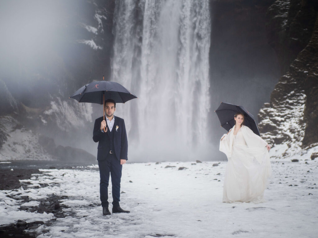 bride and groom with umbreallas by the waterfall in iceland