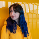 girl with blue hair posng in front of yellow wall